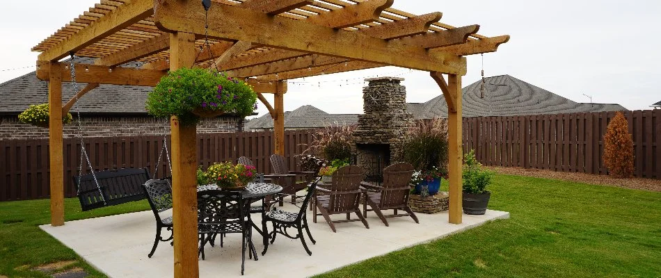 Concrete patio in Hobbs Island, AL, with a fireplace, chairs, and pergola.